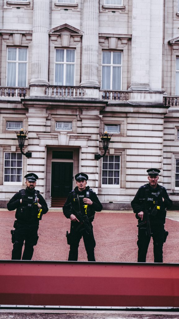 Three armed police officers stood in front of a building looking at the camera